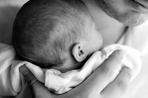Black and white photo of a newborn baby cradled in father's arms, showing tender parent-child bonding moment.
