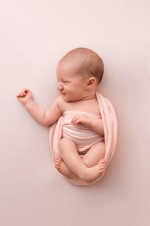 Newborn baby wrapped in a soft pink swaddle, lying peacefully on a pink background in a professional photo.