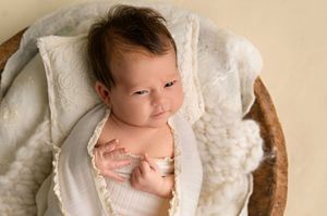 Newborn baby resting in a wooden bowl with white lace wrap during a professional newborn photography session.