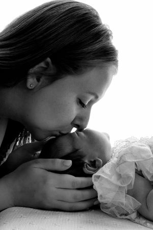 Black and white photo of a mother tenderly kissing her newborn baby, cradling the infant gently in her hands.
