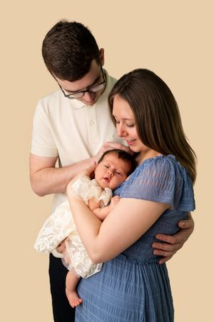 New parents tenderly cradling their sleeping newborn baby, studio portrait on beige background.