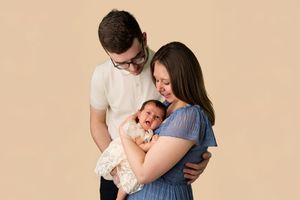 New parents lovingly gaze at their newborn baby during a professional studio portrait session with a beige background.