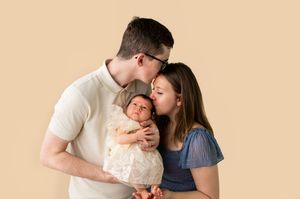 Parents kissing their newborn baby during a professional studio portrait session on a beige background.