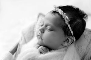 Black and white newborn photo of a sleeping baby girl wearing a delicate floral headband.
