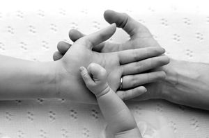Black and white photo of adult hands gently holding a tiny newborn baby hand, symbolizing love and family bond.