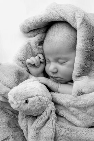 Peaceful newborn baby sleeping wrapped in soft fluffy blanket with a small stuffed animal toy, black and white photo.