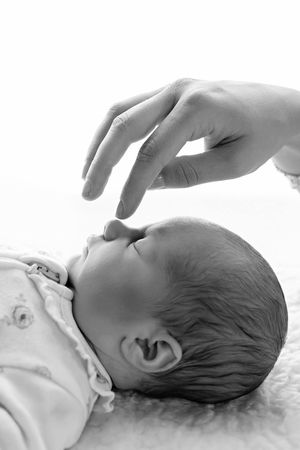 Black and white photo of a newborn baby lying down as an adult hand gently touches its nose.