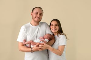 Happy couple in white t-shirts holding their newborn baby against a beige background.