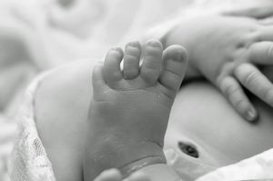 Close-up black and white photo of a newborn baby's tiny feet and hands resting on a soft white blanket.