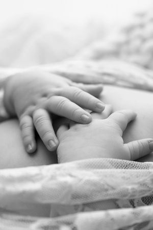 Black and white close-up of a newborn baby's tiny hand resting gently on an adult's hand.