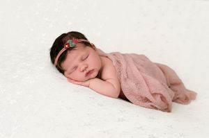Peaceful newborn baby girl sleeping wrapped in pink swaddle with floral headband on white background.