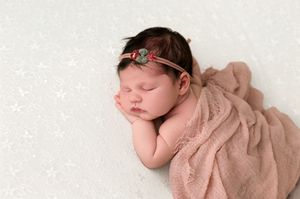Sleeping newborn baby girl wrapped in a soft pink lace blanket with a floral headband on a white background.