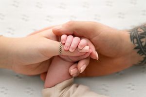 Two adult hands gently cradling a newborn baby's tiny hand, symbolizing love and family bonding.