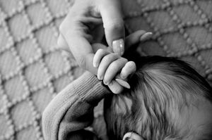 Black and white photo of a newborn baby grasping an adult finger, symbolizing new life and parent-child bond.
