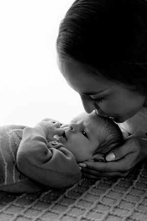 Black and white photo of a mother tenderly kissing her newborn baby on the nose while cradling its head.