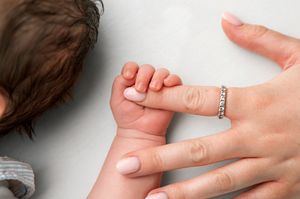 Newborn baby grasping mother's finger wearing a diamond ring in a tender close-up photo.