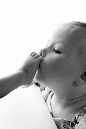 Black and white photo of a cute baby sucking on their own tiny foot, close-up portrait.