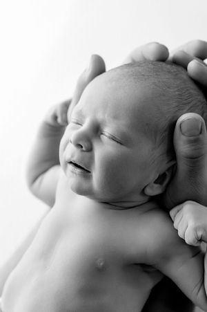 Black and white photo of a crying newborn baby being gently held by adult hands.