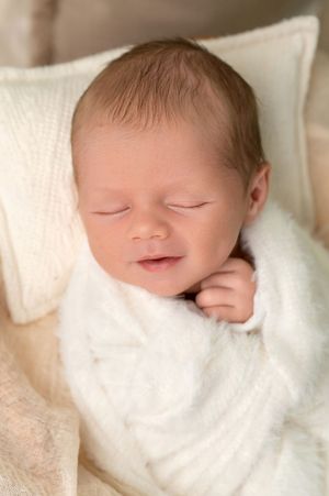 Peaceful newborn baby sleeping soundly wrapped in a soft white blanket, with tiny fist visible.