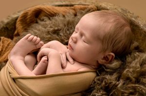 Peaceful newborn baby sleeping curled up in a rustic wooden bowl with soft brown fur blanket in a studio portrait.