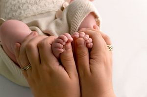 Close-up of parents hands gently holding newborn baby feet, with mother wearing gold rings.