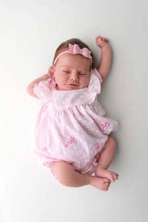 Sleeping newborn baby girl in pink floral romper and bow headband lying on white background.