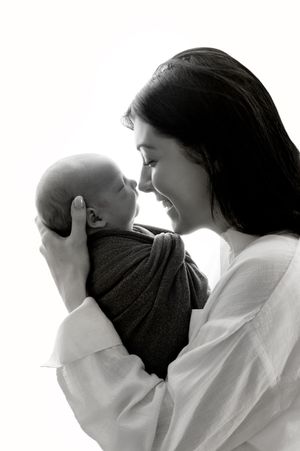 Black and white photo of a smiling mother tenderly holding her swaddled newborn baby close to her face.