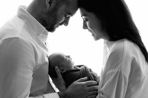 Black and white photo of parents smiling at their newborn baby held tenderly between them.