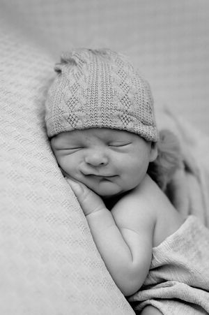 Black and white photo of a sleeping newborn baby wearing a knit hat, peacefully resting on a soft blanket.