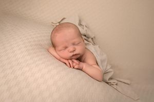 Peaceful newborn baby sleeping on a soft beige blanket, wrapped in a light gray swaddle, hands tucked under chin.
