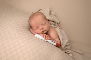 Newborn baby sleeping peacefully on beige blanket holding a pregnancy test, soft neutral tones.