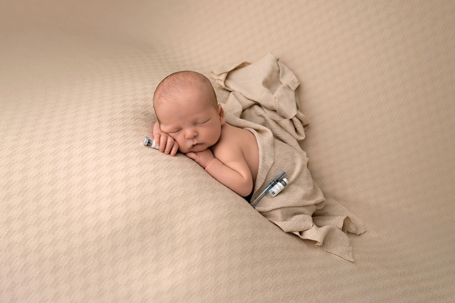 Newborn baby sleeping peacefully wrapped in a soft beige blanket on a cream textured background.