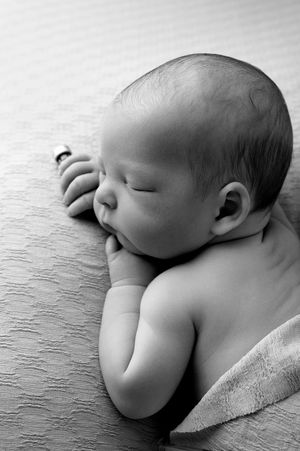 Black and white photo of a peaceful sleeping newborn baby resting on a soft textured blanket.