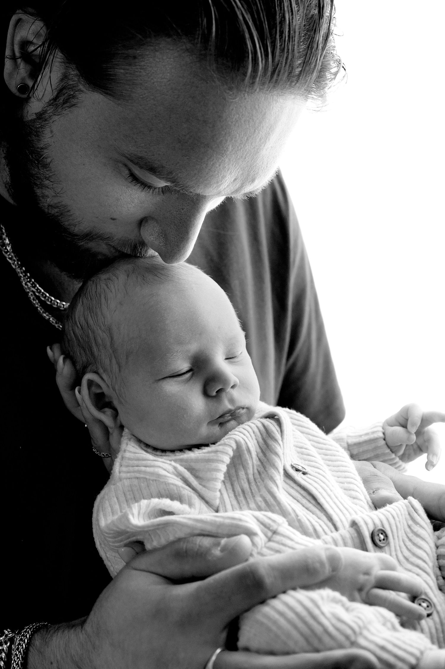 Black and white photo of a father tenderly kissing his sleeping newborn baby on the forehead.