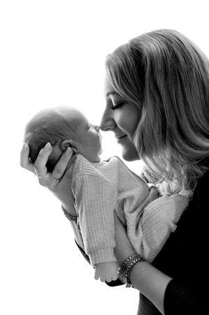 Black and white photo of a smiling mother holding her newborn baby close, touching noses in a tender moment.