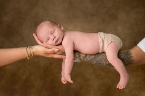 Newborn baby sleeping peacefully on outstretched hands of parents against brown background.