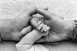 Black and white photo of a newborn baby's tiny hand grasping an adult's fingers, symbolizing love and family bond.