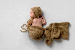 Newborn baby sleeping peacefully wrapped in a soft brown fuzzy blanket and matching bear bonnet on white background.