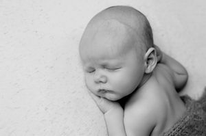 Black and white newborn baby sleeping peacefully on soft blanket, eyes closed, tiny hands tucked under cheek.