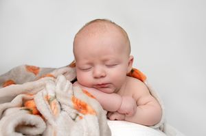 Newborn baby sleeping peacefully on a soft blanket with orange patterns against a white background.