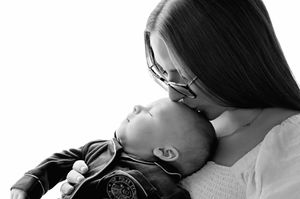 Black and white photo of a mother gently kissing her newborn baby on the forehead in a tender moment.