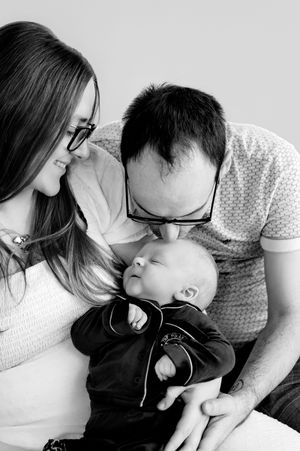 Black and white photo of parents lovingly holding and kissing their newborn baby during a family portrait session.