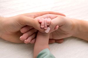 A newborn baby's tiny hand grasping an adult's fingers, symbolizing love, family bond, and new parenthood.