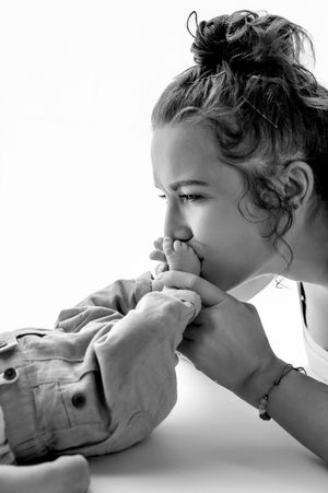 Black and white photo of a young girl with curly hair kissing a baby's tiny feet tenderly.