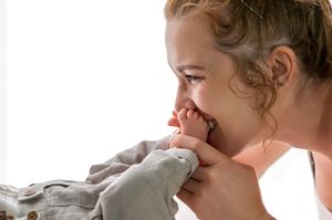 A young girl smiles while kissing a baby's tiny feet, sharing a tender moment of sibling affection.