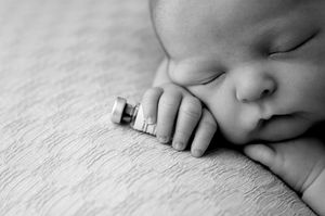 Black and white photo of a sleeping newborn baby holding a small toy car in tiny hands.