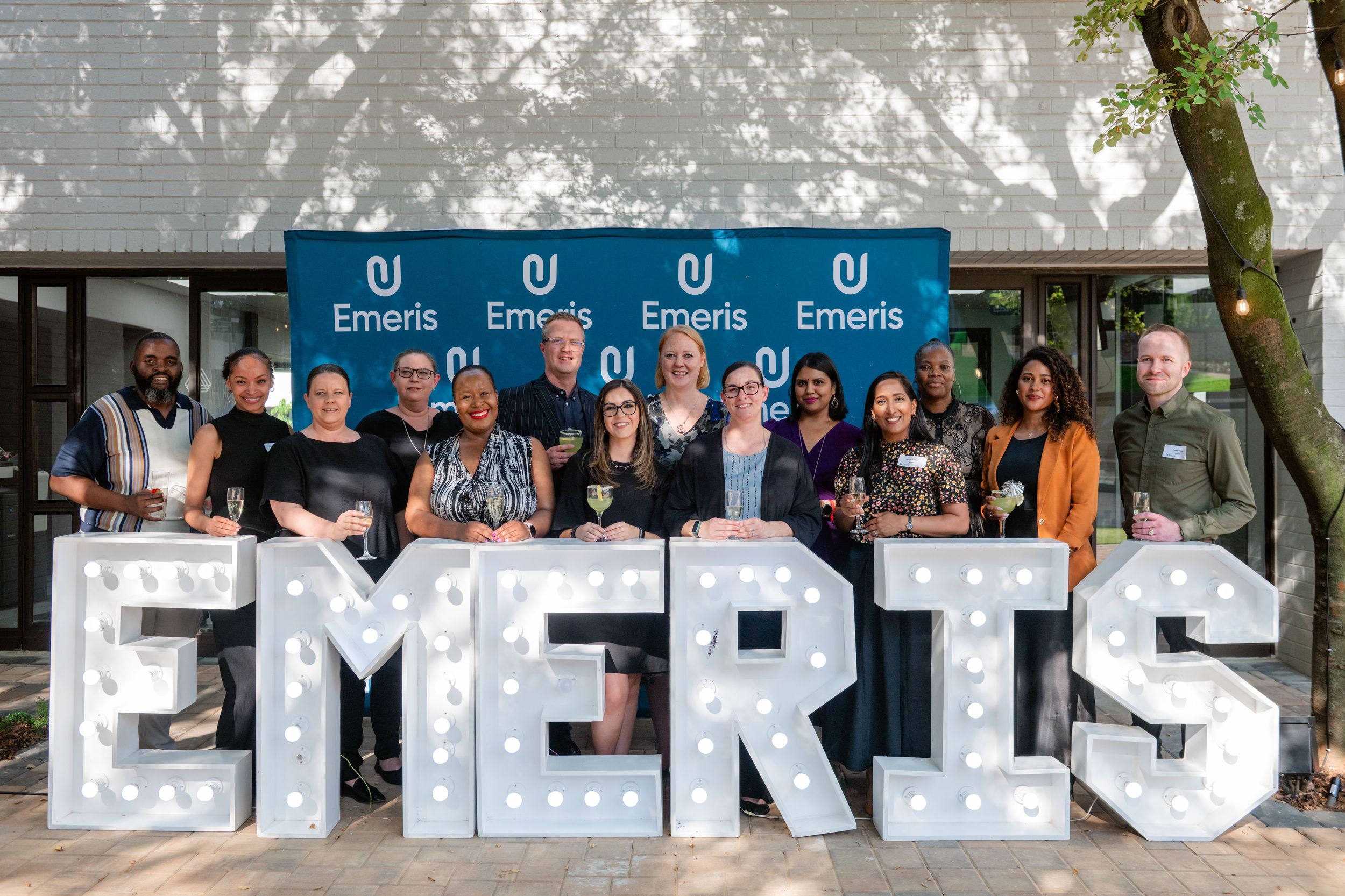 Large group celebrating together behind the Emeris sign at Sandton Campus.