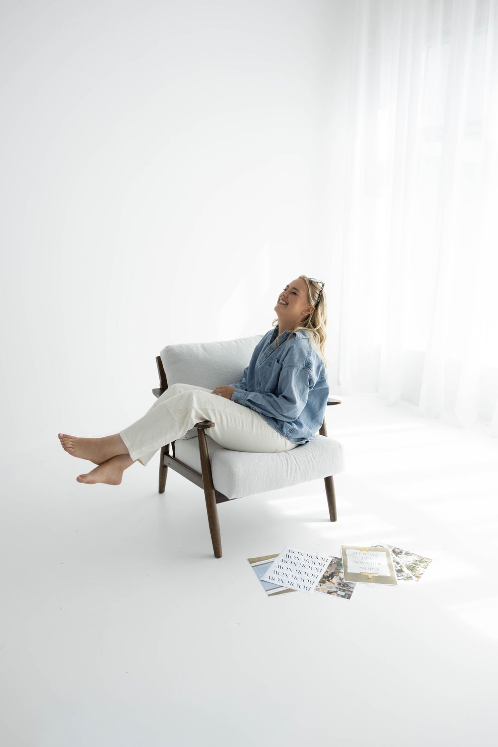 Woman in denim shirt and white pants relaxing in a mid-century modern armchair with design samples on the floor.