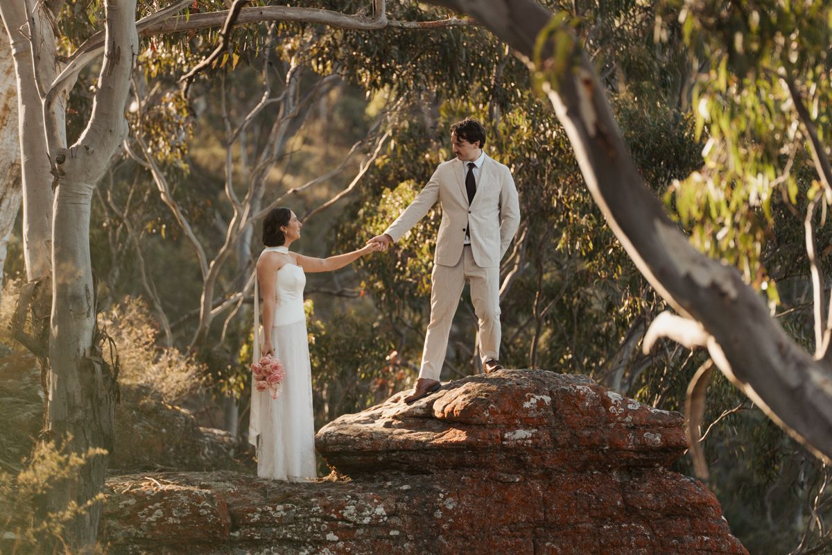 Bride and groom hold hands on a rocky outcrop surrounded by eucalyptus trees in an outdoor bush elopement ceremony blue mountains