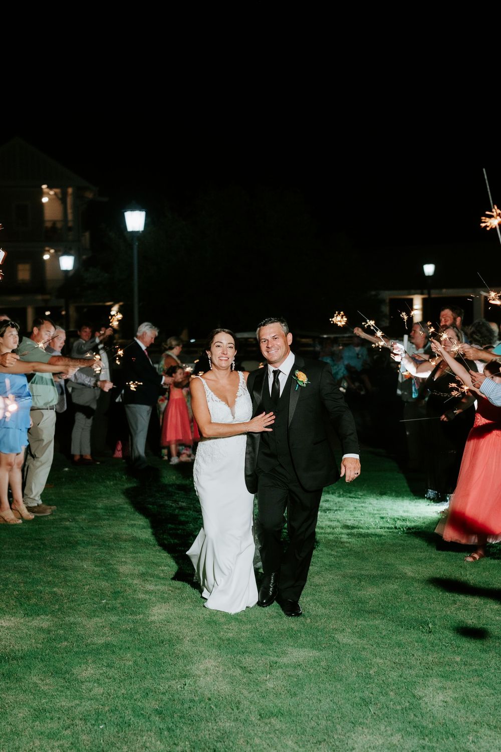 Bride and groom walk through sparkler exit at night wedding reception outdoors.